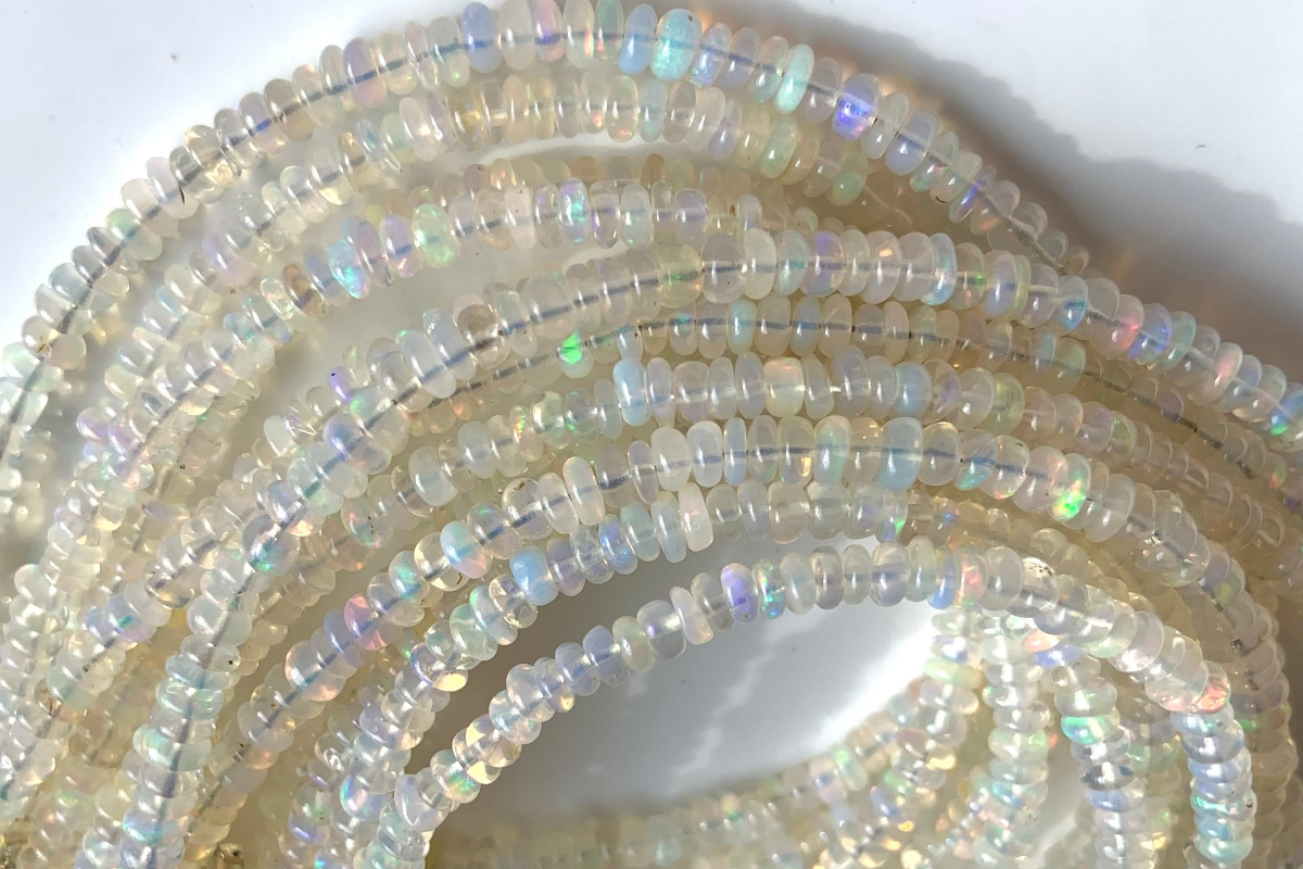 Closeup of luminous white opal bracelets arranged in a rainbow arc — translucent beads flash with rainbow fire. October birthstone crystal jewelry for healing, transformation, and divine connection.