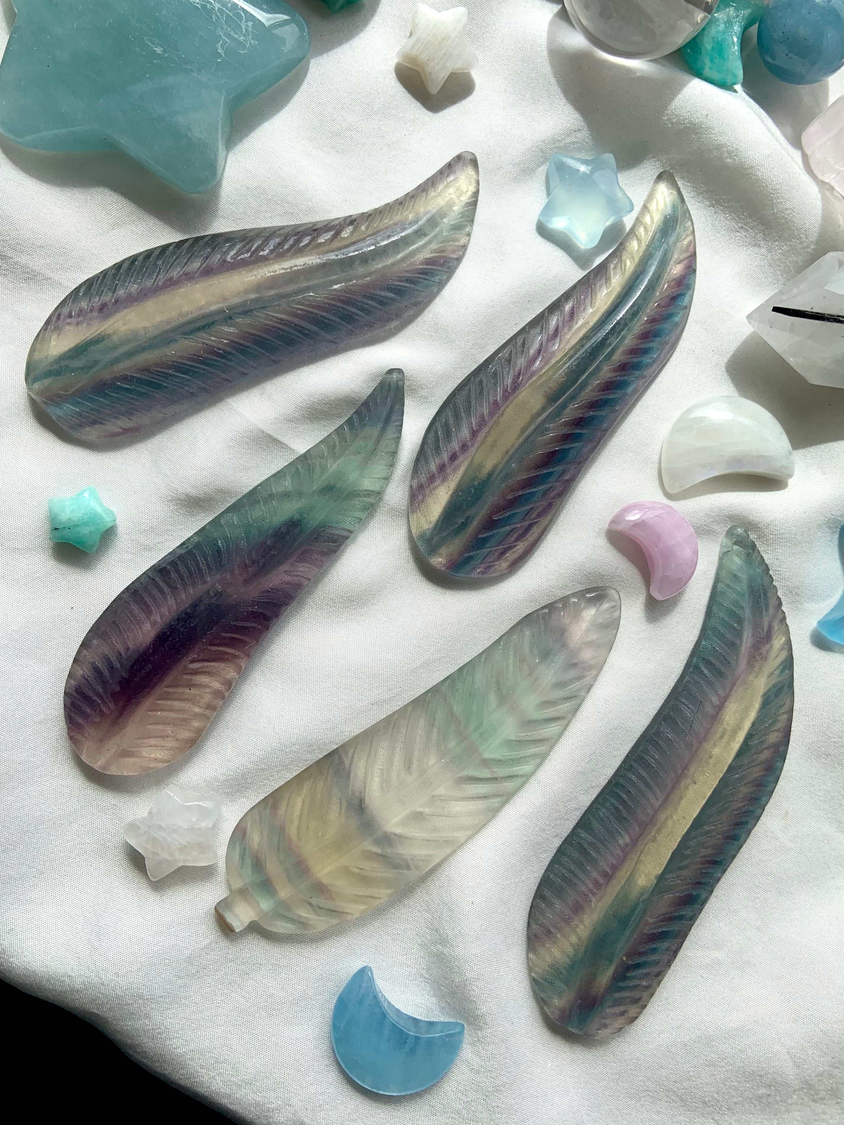 Fluorite feather crystal carvings in calming blue-green hues arranged with celestial stones in an inviting, spiritual display.