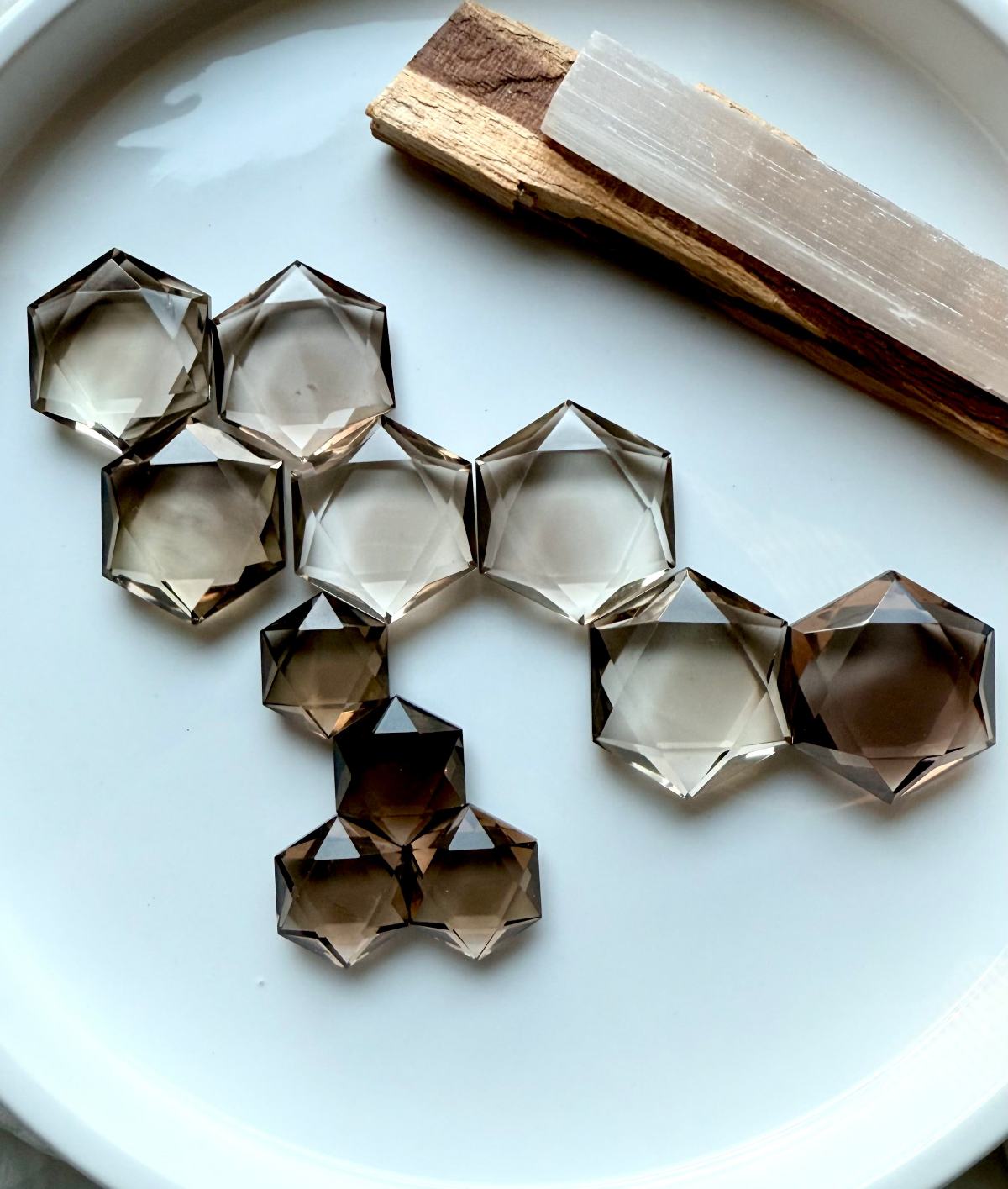 Smoky Quartz hexagon crystals arranged on white plate with selenite and palo santo, grounding crystal collection for protection and emotional balance