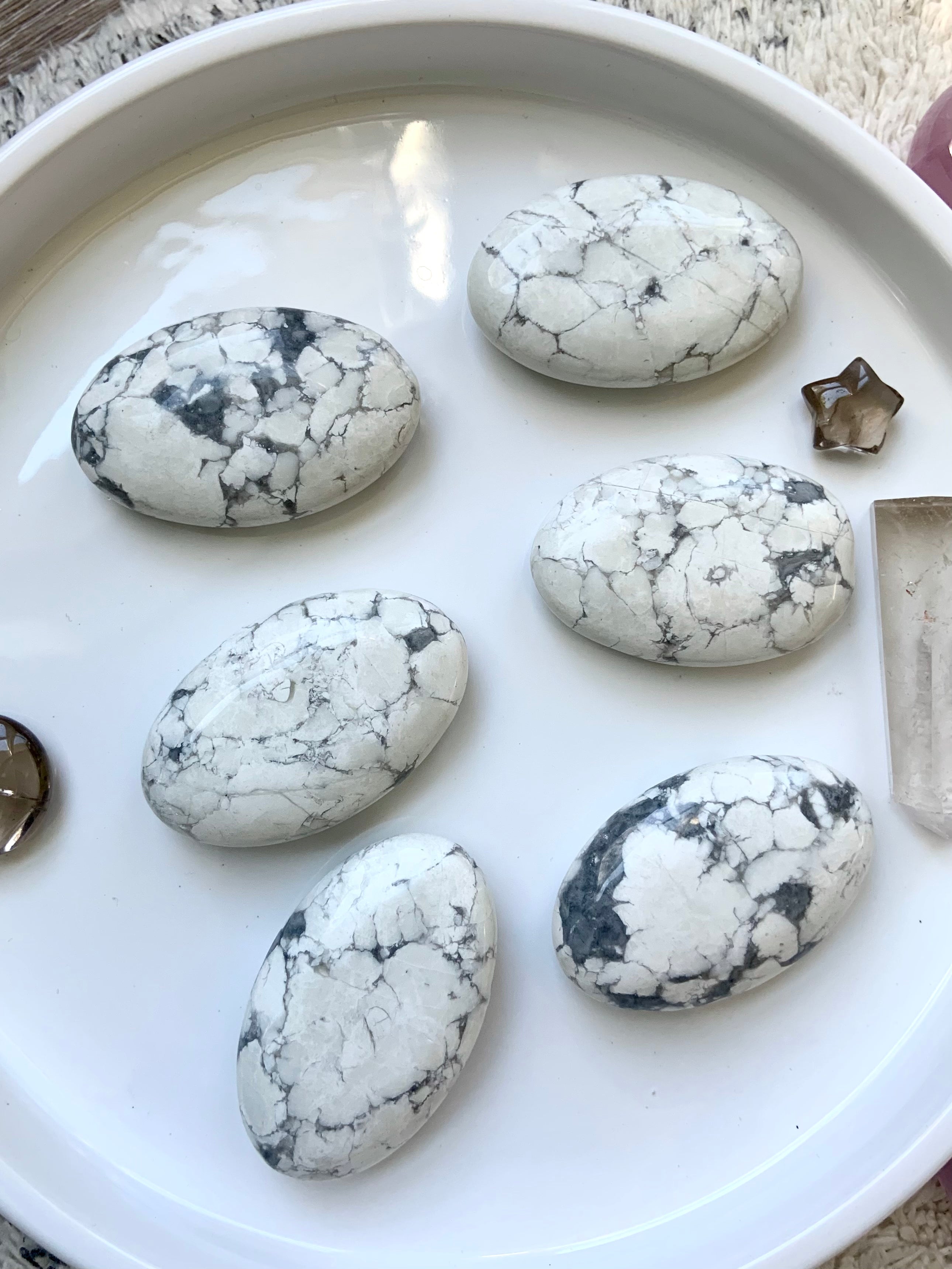 White Howlite crystal palm stones with gray veining displayed in a white dish, polished for meditation, chakra healing, and calming energy.