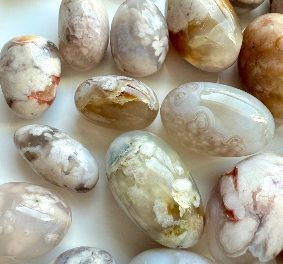 High-quality Flower Agate tumbled stones in a variety of colors and patterns, showing natural blooms, banding, and translucent chalcedony, crystal array on white background.