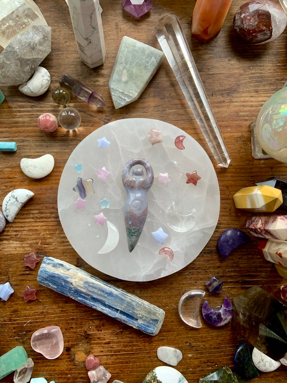 An ocean jasper crystal goddess carving on a selenite plate with celestial crystals all around