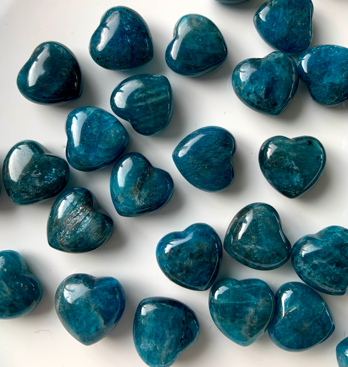 Shimmery Blue Apatite crystal hearts with natural chatoyancy on white background — radiant stones for Throat and Third Eye Chakra healing.