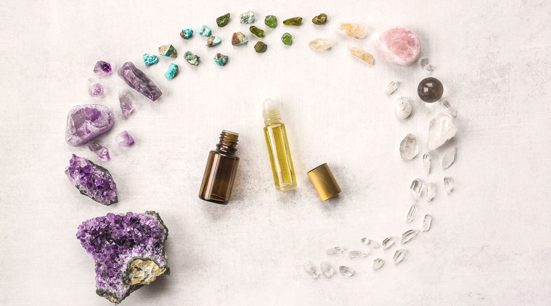 Crystal-infused roller bottle surrounded by a rainbow arc of healing stones — gemstone elixir for aura cleansing, ritual anointing & high-vibrational self-care.