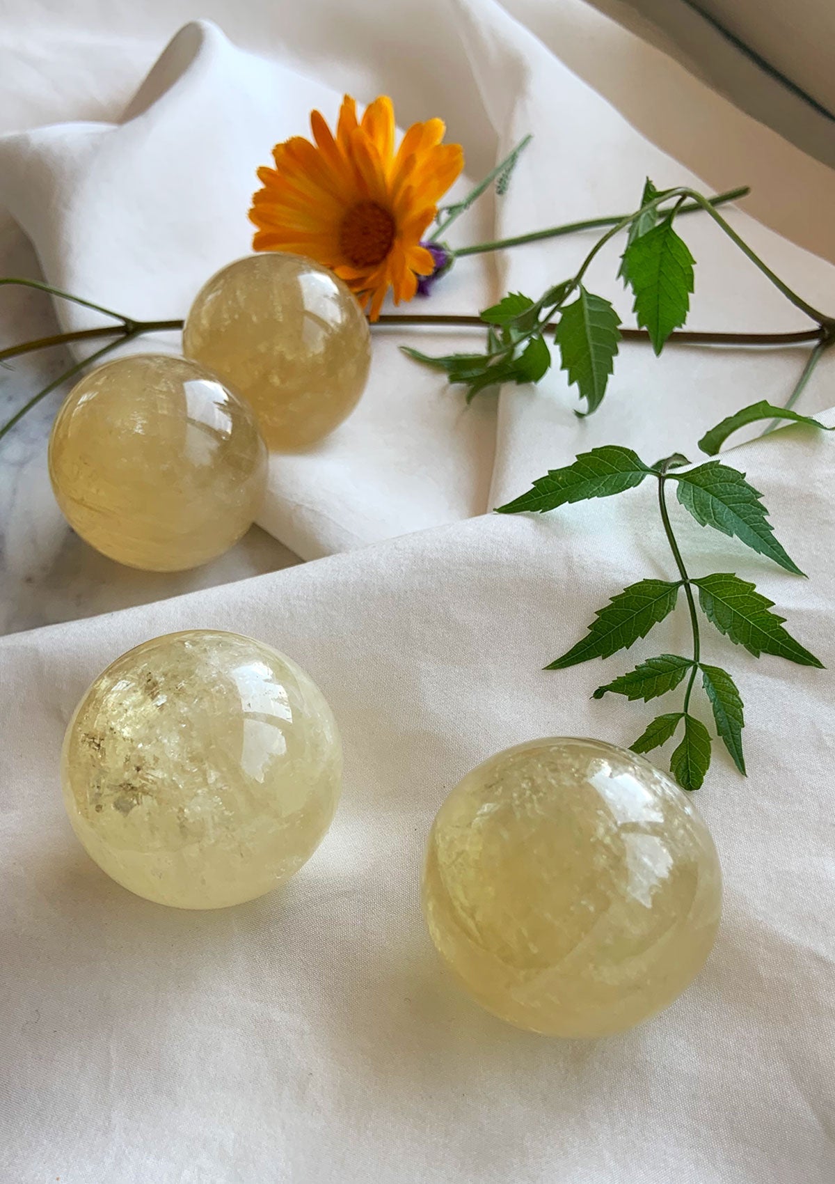 Golden Honey Calcite spheres on white silk with a green vine, arranged to frame the composition — high-quality Calcite crystals for chakra balance, clarity, and spiritual vitality