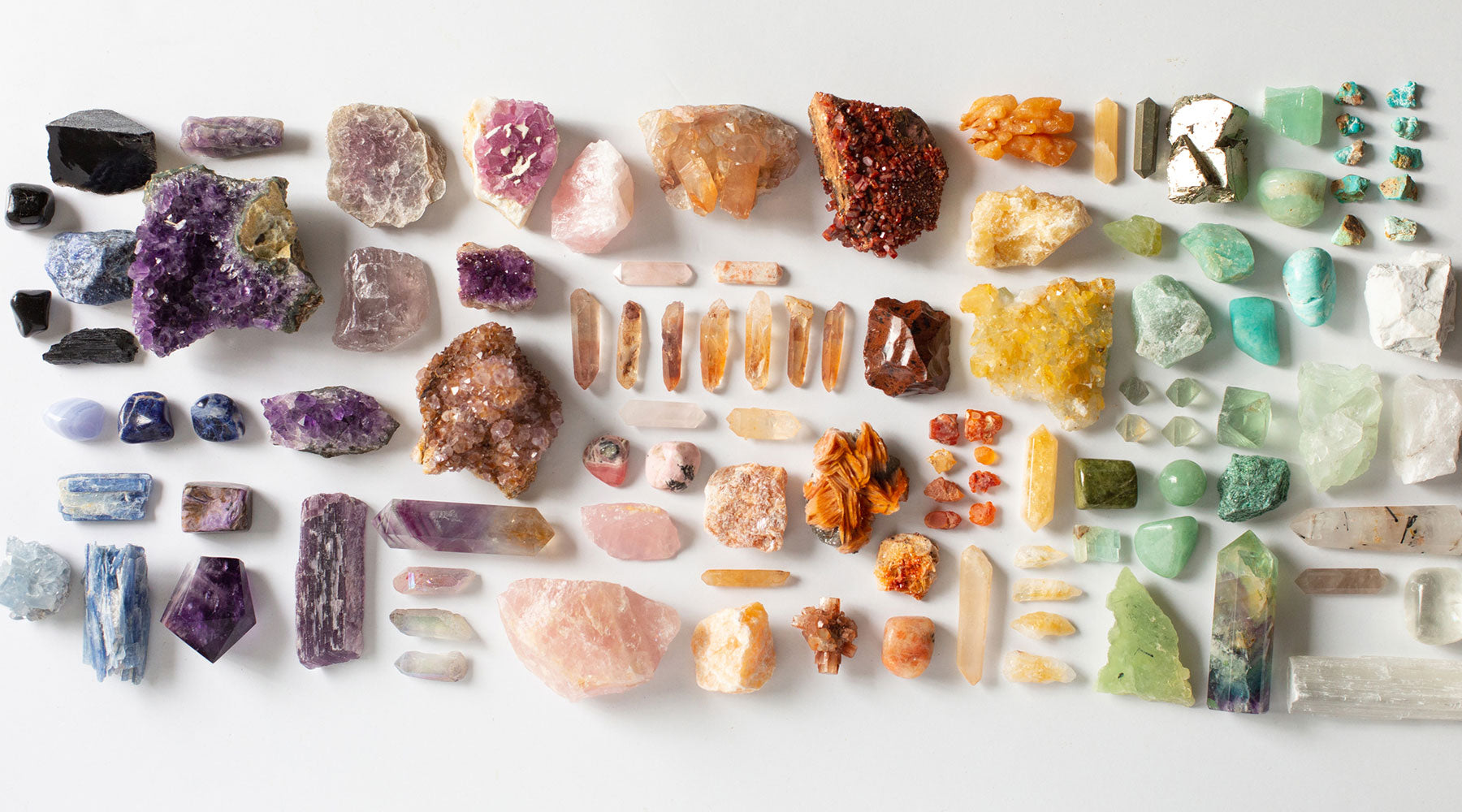 Rainbow crystal grid flatlay featuring over 100 raw and polished crystals arranged by color — a curated collection of high-vibe stones for energy healing, chakra alignment, and spiritual growth.