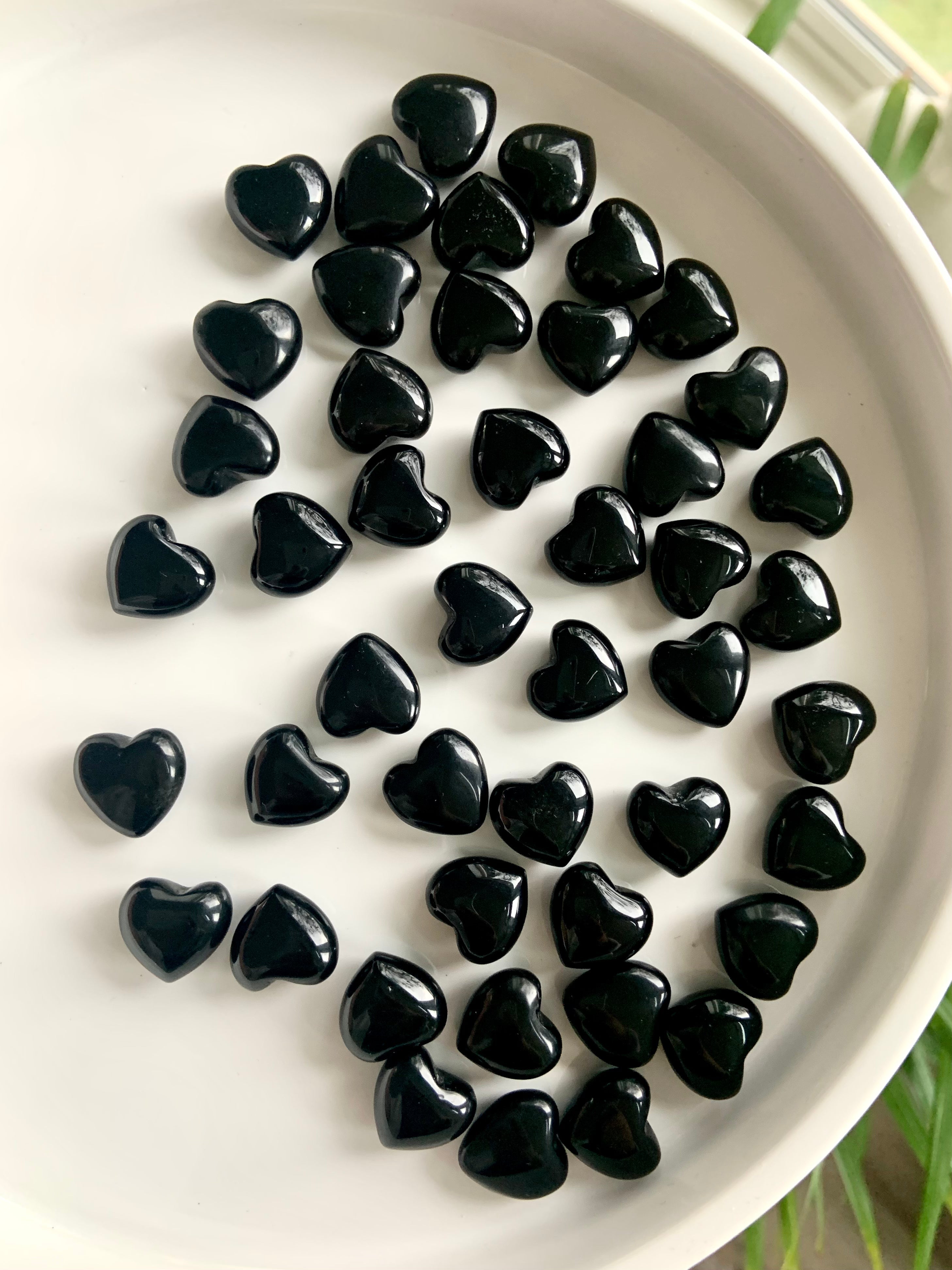 An array of tiny black obsidian hearts shown on a white plate