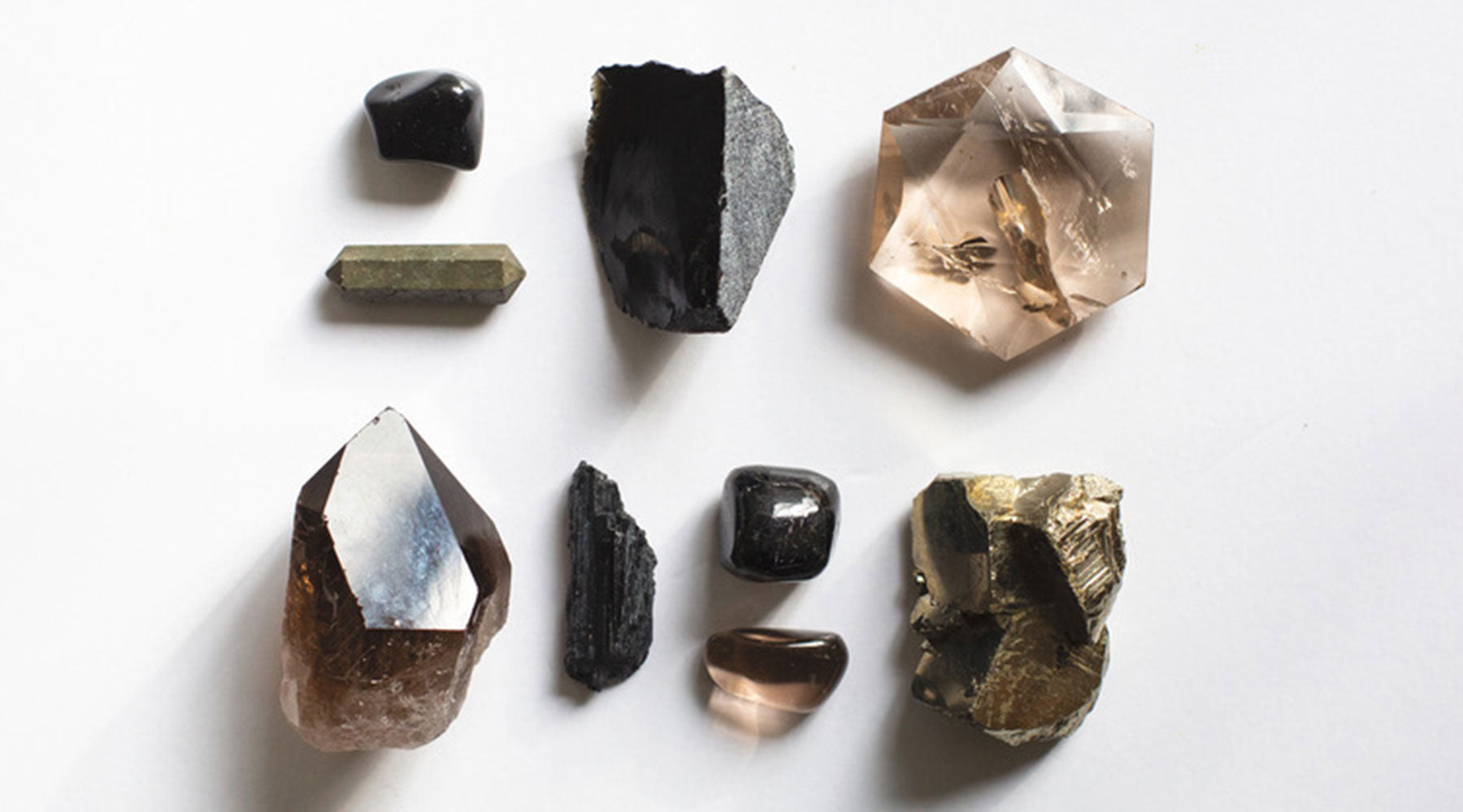 Flatlay of Root Chakra crystals including Smoky Quartz, Black Obsidian, Jet, Pyrite, and Black Kyanite — grounding stones for protection and stability.