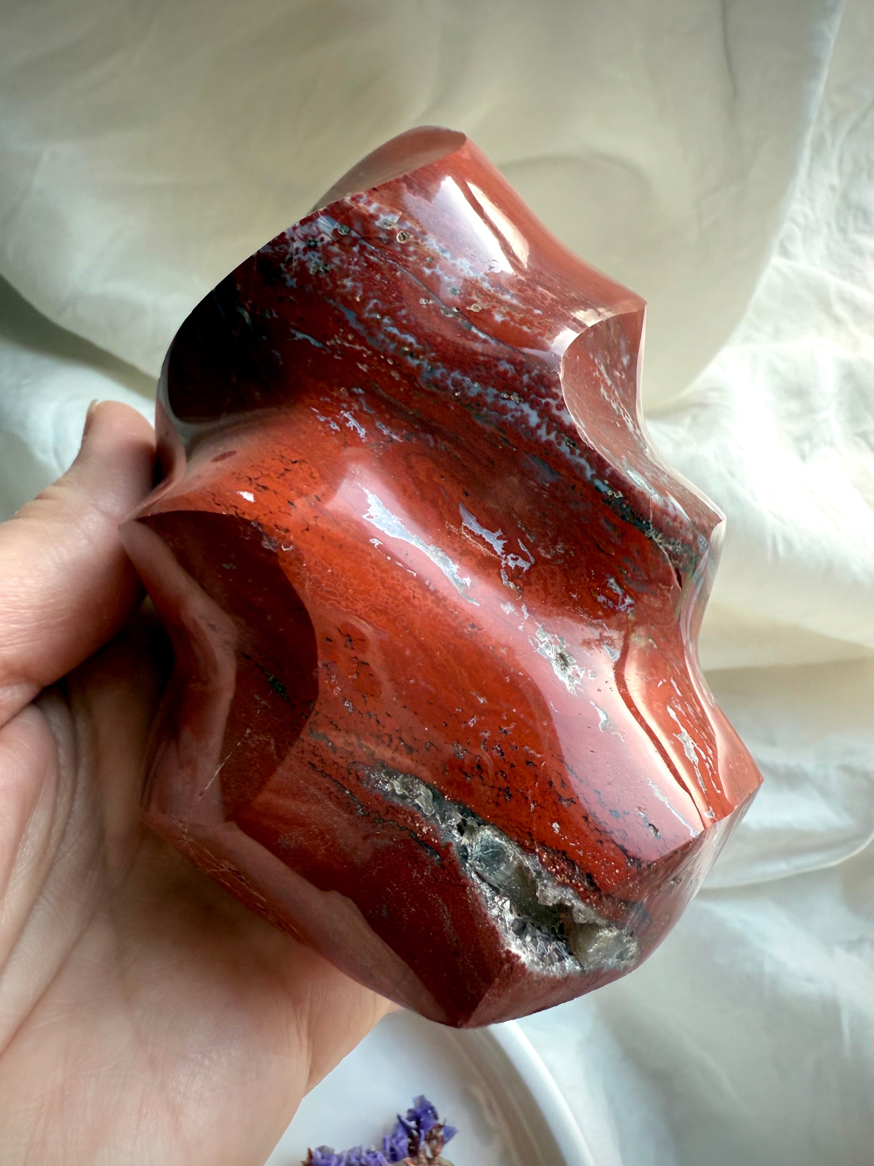 Red Ocean Jasper flame carving photographed in natural window light with deep red bands and subtle druzy inclusions.