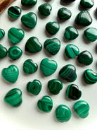 Close-up of polished Malachite heart carvings showing rich banded patterns in vibrant green tones.