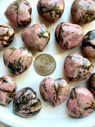 Rhodonite heart carvings with natural black manganese matrix and unique pink stone patterns shown with a US quarter for scale