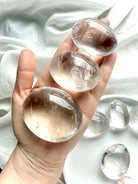 three clear quartz palm stones held in hand with high clarity, silvery flashes, and natural inclusions