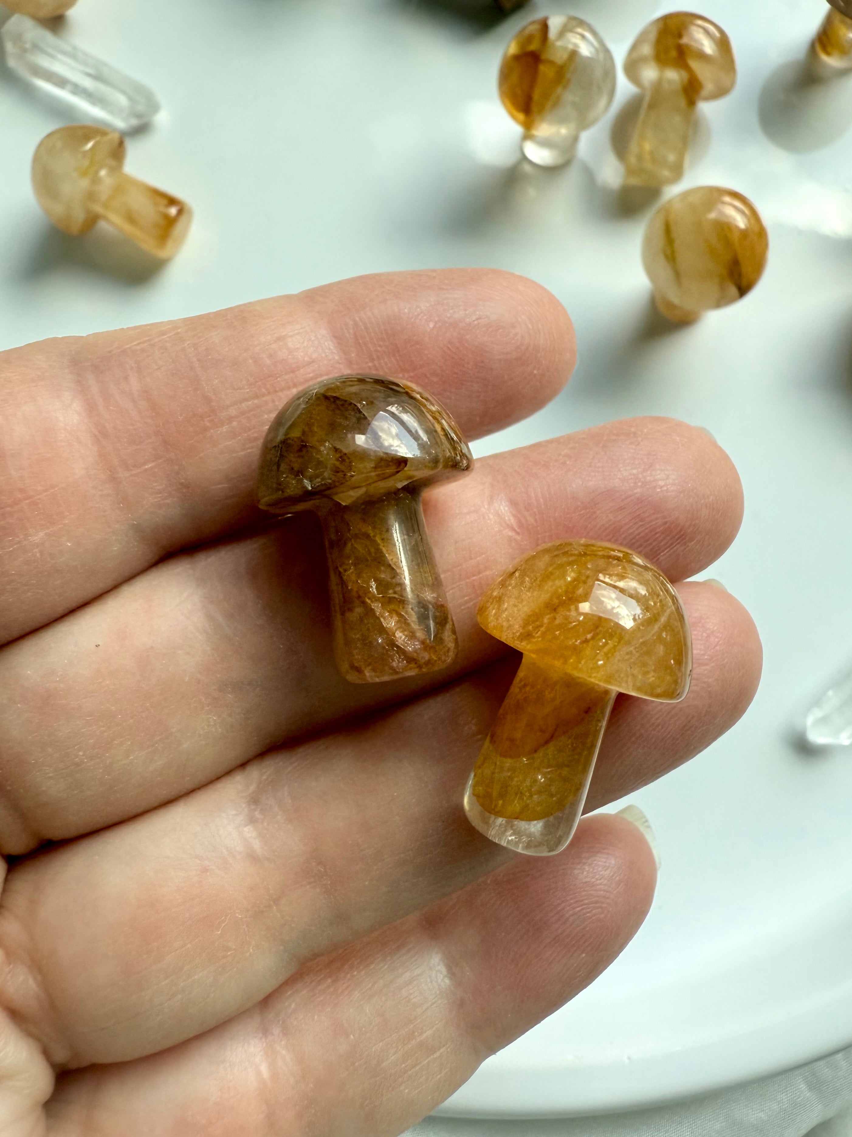 Closeup of two Golden Healer Quartz mushrooms resting in hand — crystal carvings for Solar Plexus chakra healing, confidence, and empowerment.