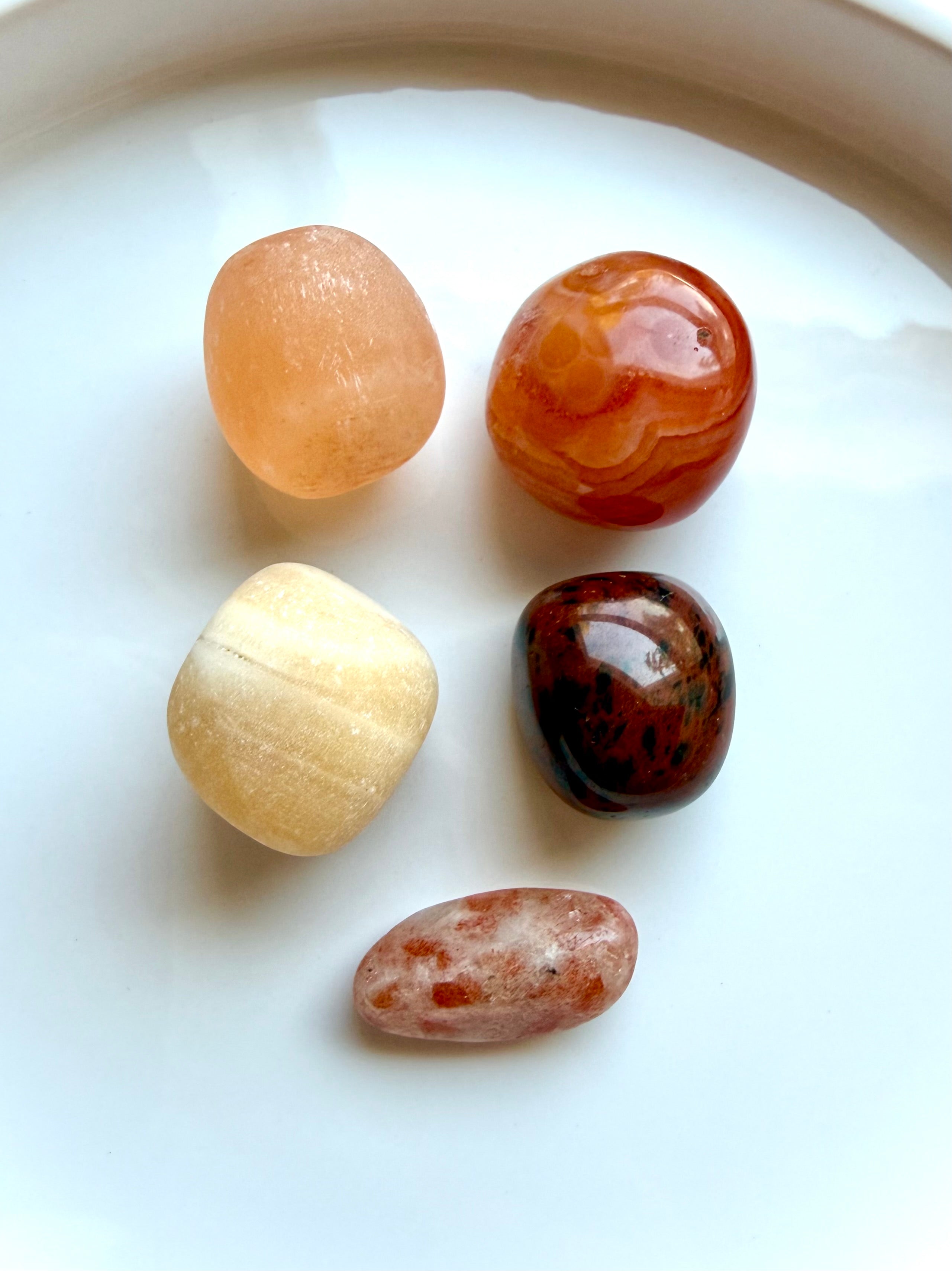 Five polished Sacral Chakra stones including Orange Calcite, Carnelian, Peach Selenite, Mahogany Obsidian, and Sunstone