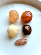 Five polished Sacral Chakra stones including Orange Calcite, Carnelian, Peach Selenite, Mahogany Obsidian, and Sunstone