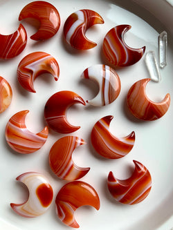 An array of Banded Carnelian Crescent Moons shown in natural light on a white plate with some other crystals as accents