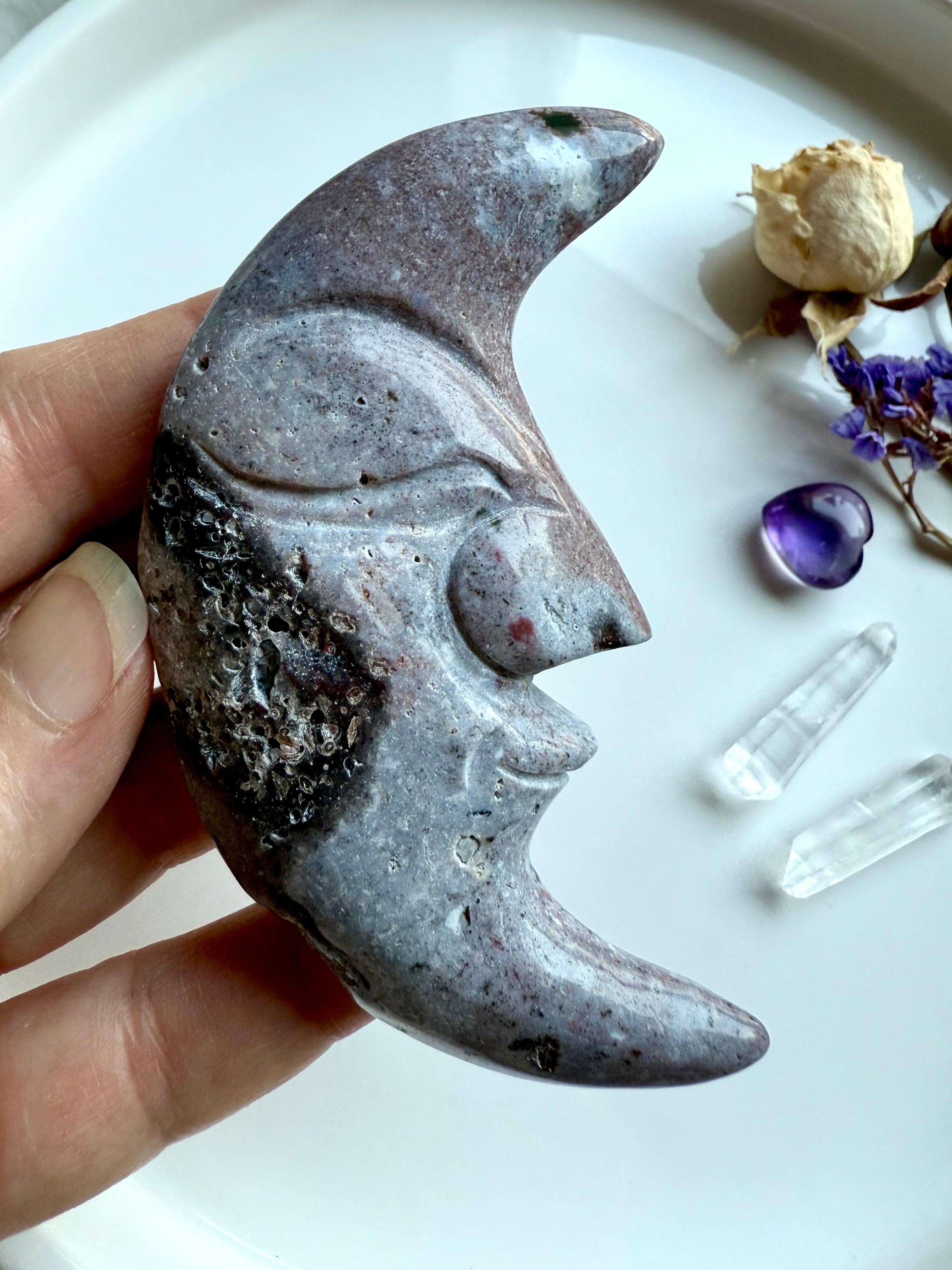 Purple Ocean Jasper moon face crystal with druzy detail, displayed beside quartz points, amethyst, and flowers.