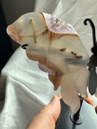 Close-up of carved agate butterfly wings with amethyst druzy edges, showing translucent banding and natural inclusions, unique crystal art piece.