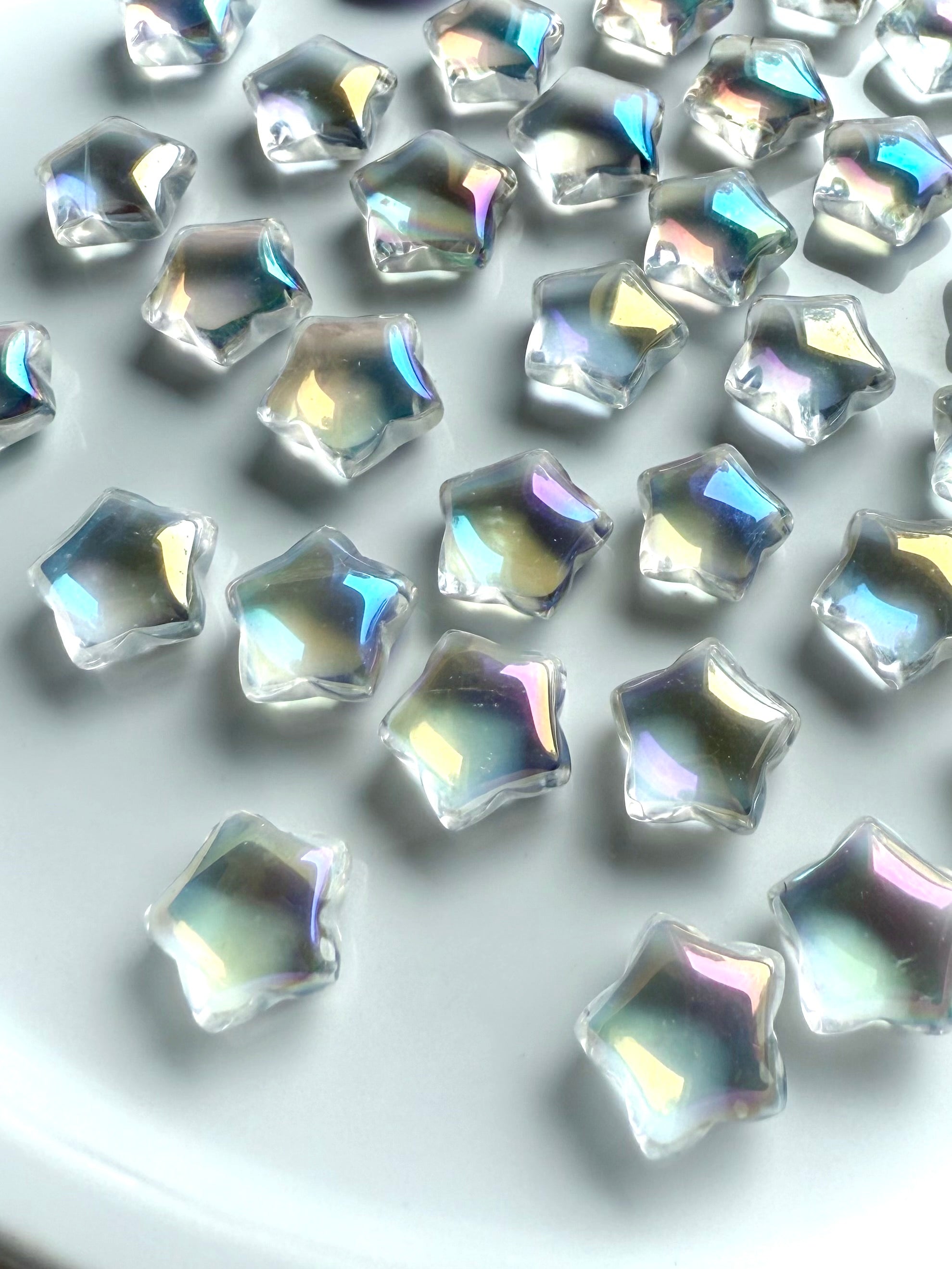 Rainbow aura quartz mini star carvings with iridescent rainbow sheen, polished crystal stars on white background for chakra healing, crystal grids, and altar décor