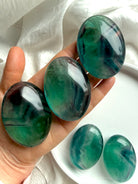 Three large teal fluorite palm stones held in hand for scale with additional blue green banded stones in background