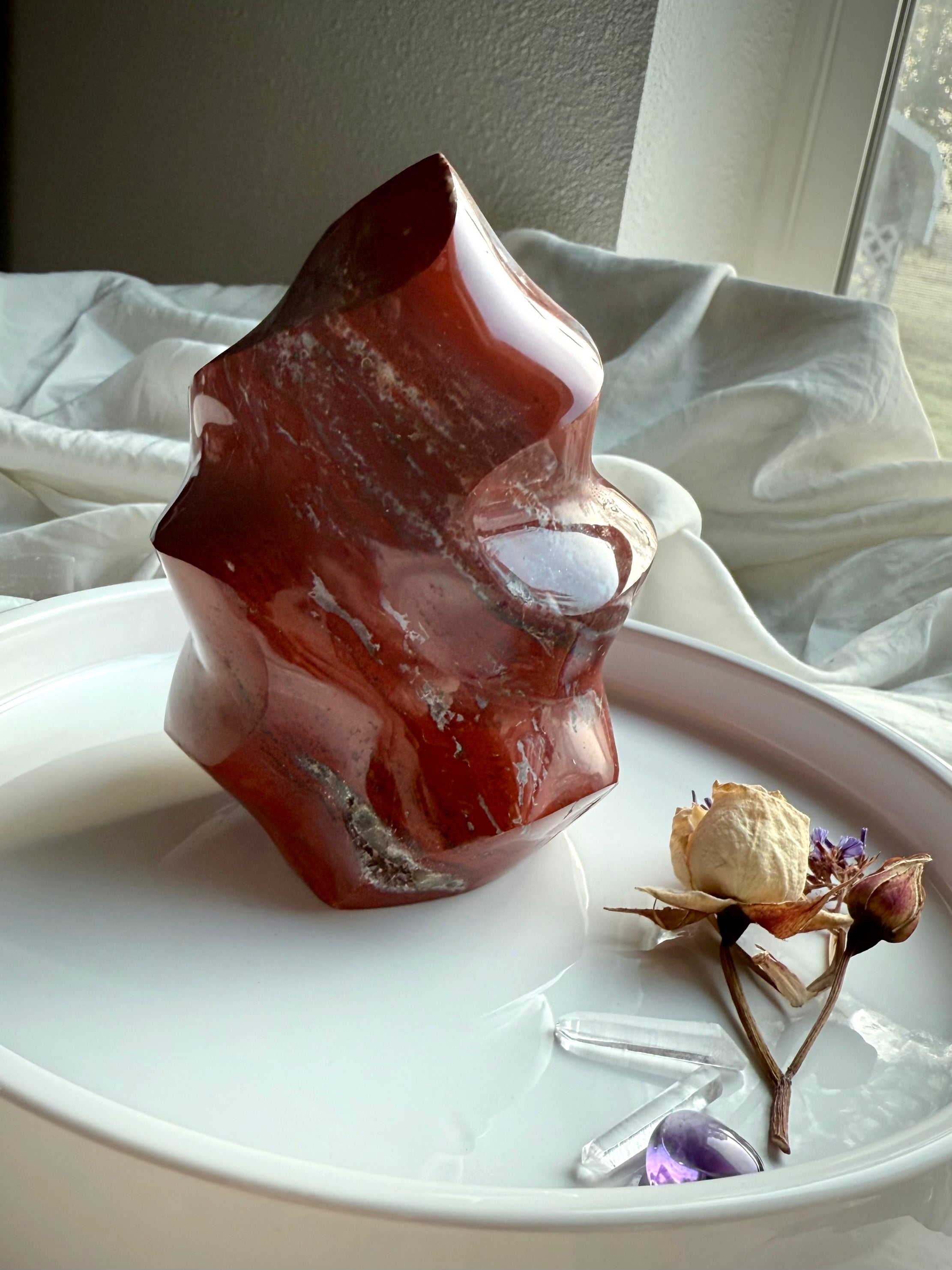 Red Ocean Jasper crystal flame displayed on a white tray with dried flowers and quartz points.