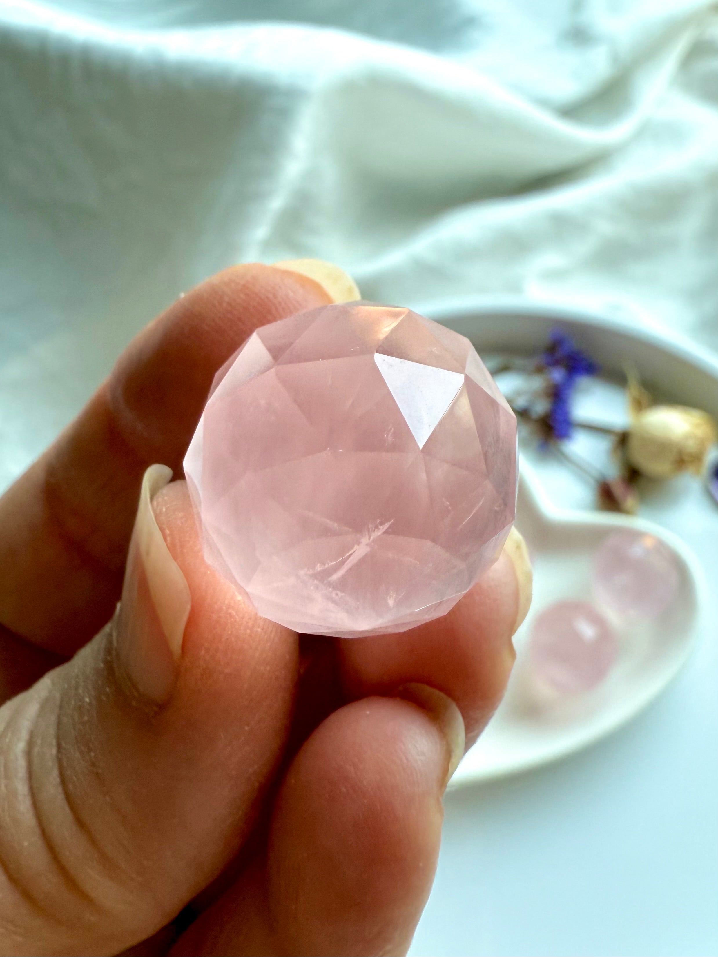 Closeup of a hand showing the intricate details of a mini faceted rose quartz crystal ball.