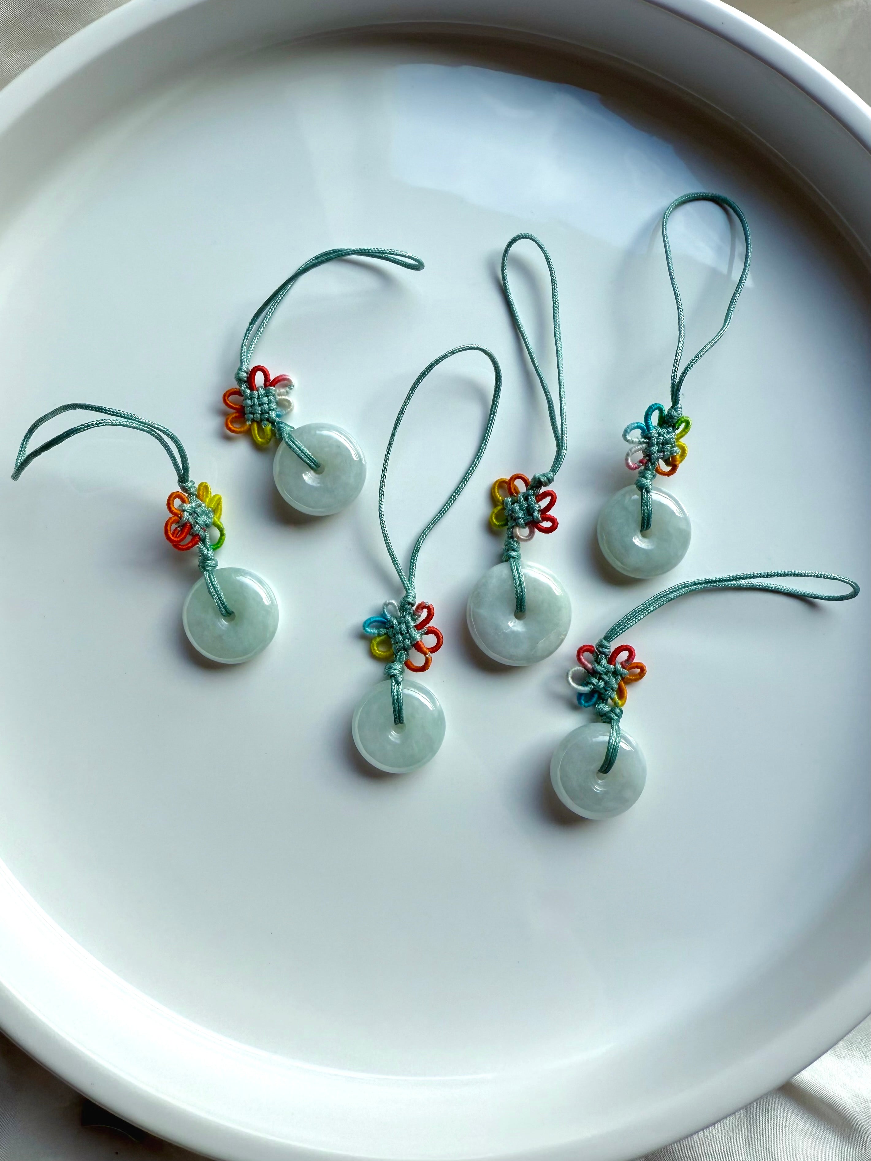 Natural jade donut talismans with rainbow flower knots displayed in a crescent fan shape 