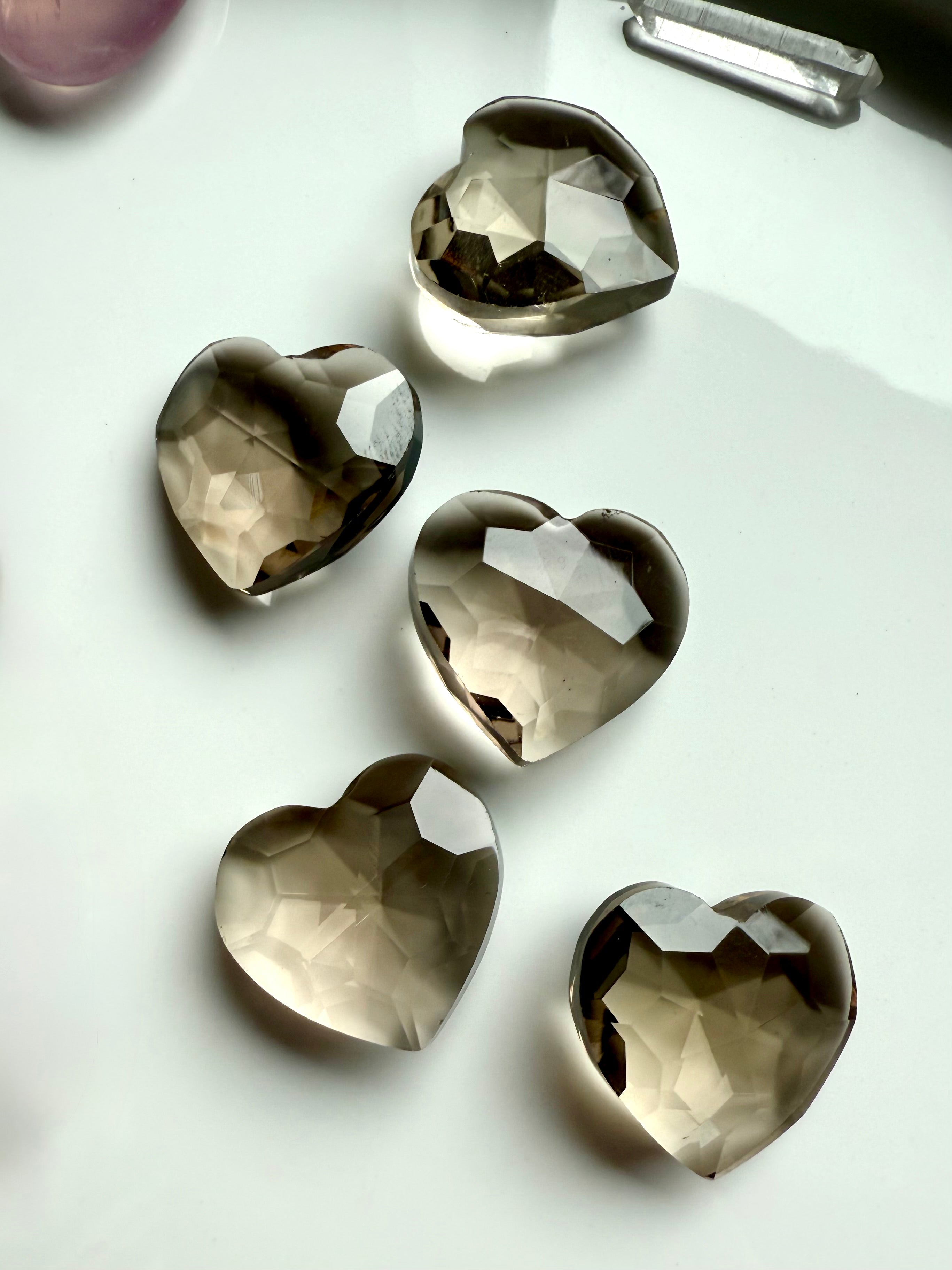 Smoky Quartz crystal hearts arranged on a white background — faceted Root Chakra crystals for grounding, energy clearing, emotional healing, and protection.