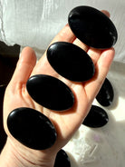 Black Obsidian palm stones resting in hand showing smooth polished volcanic glass and rich jet-black luster