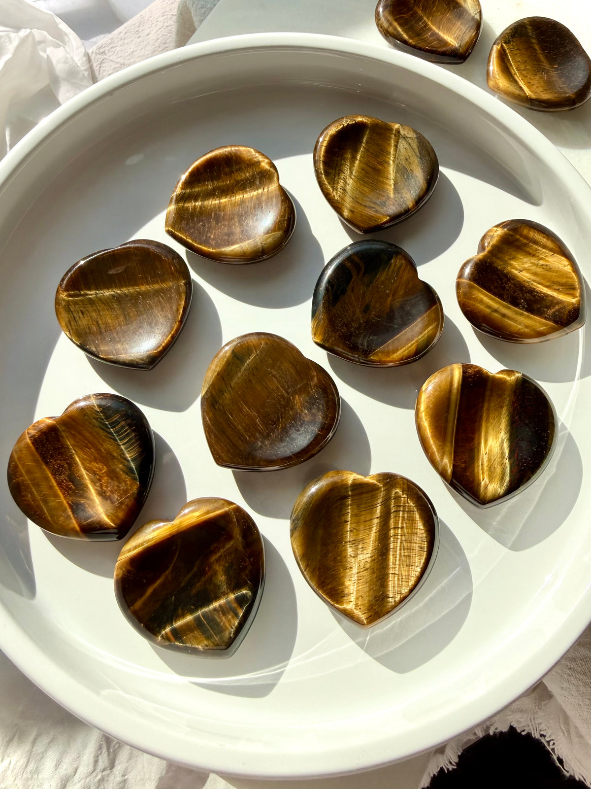 Tiger’s Eye heart worry stones arranged on a white dish, displaying varied golden, caramel, and dark brown banding