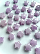 Closeup of pink Kunzite star carvings scattered on a white background, highlighting their glossy polish and soft shimmer.