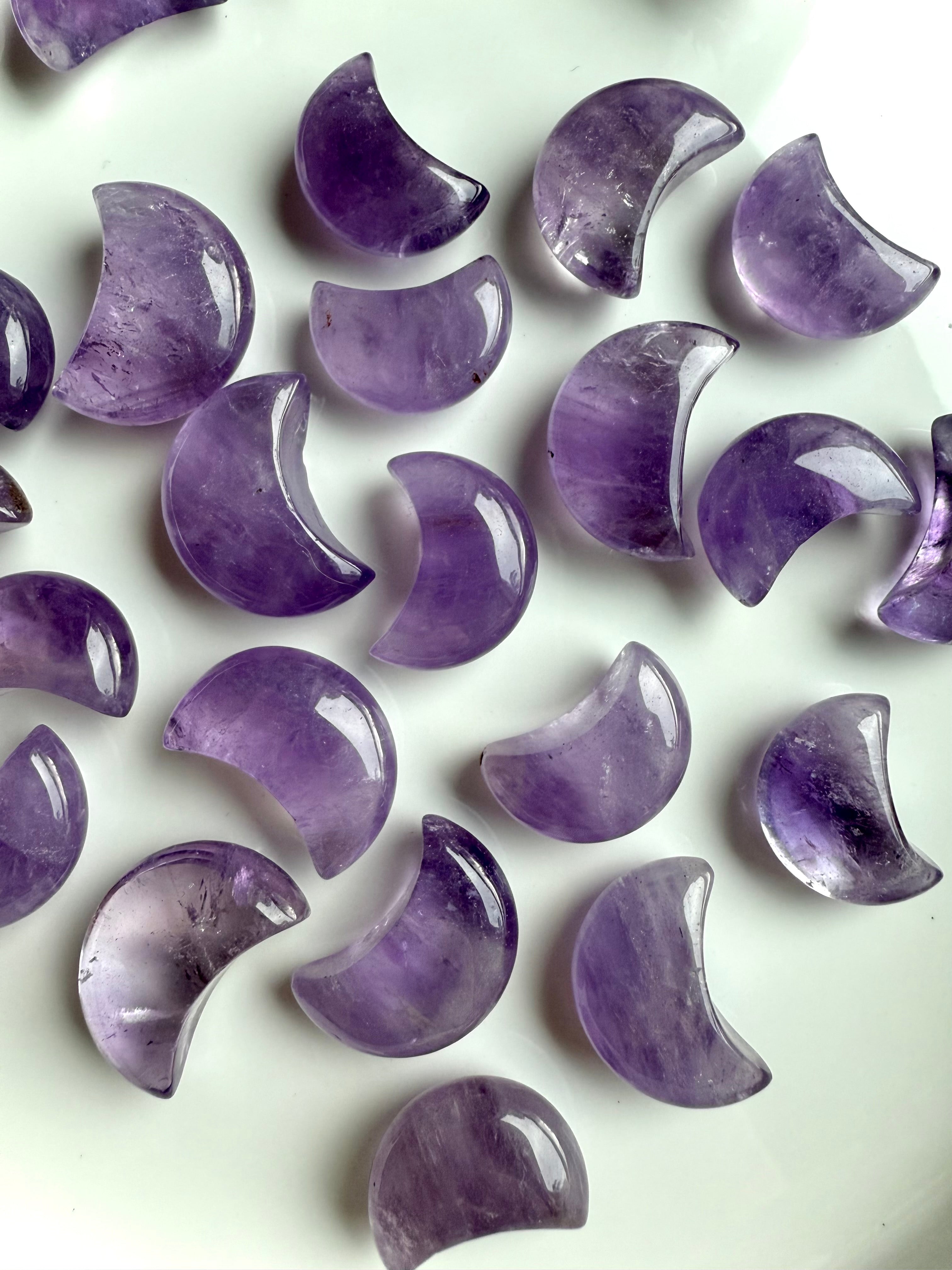 Mini amethyst crescent moon carvings in soft lavender and deep violet shades, polished crystal moons arranged on a white surface.