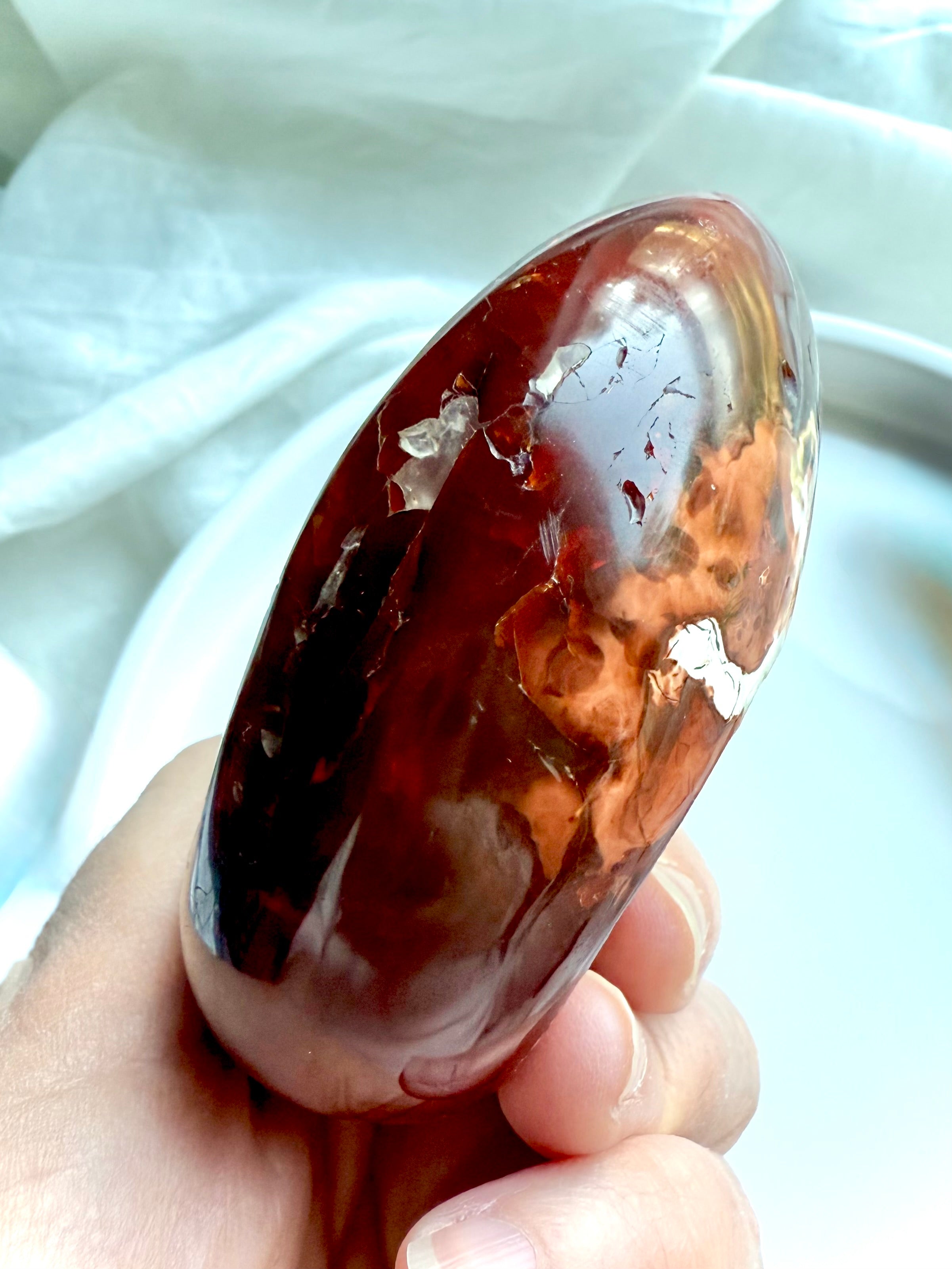 Side view of hand holding polished red carnelian crystal bowl with fiery glow and natural inclusions – healing dish for jewelry or altar 