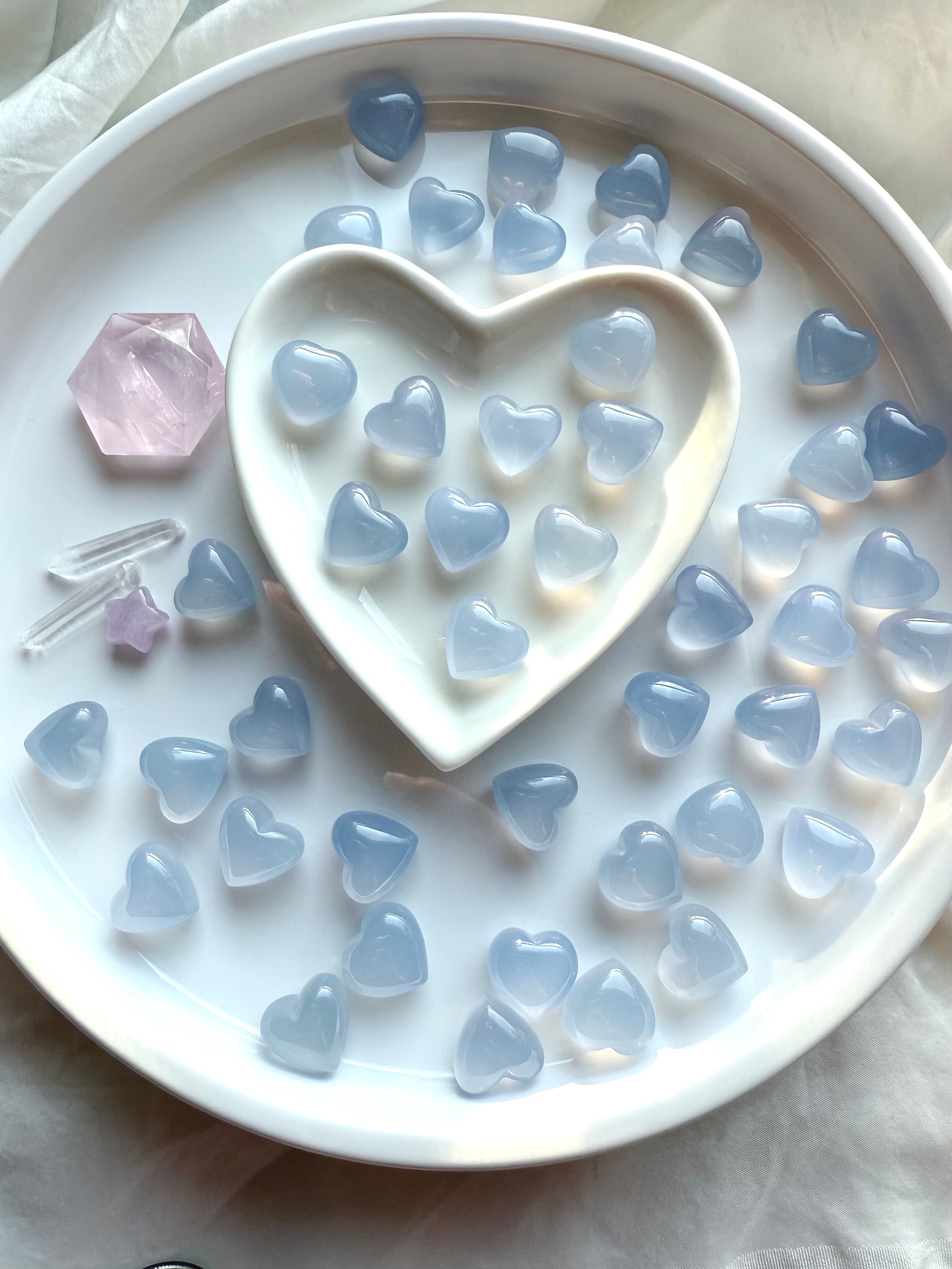 Mini Blue Chalcedony heart crystals arranged on a white ceramic tray, soft blue translucent Throat Chakra stones for calm communication and emotional balance