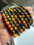Group of bumblebee jasper crystal bracelets displayed in hand, rich orange and yellow banding in natural stone beads for motivation and energy