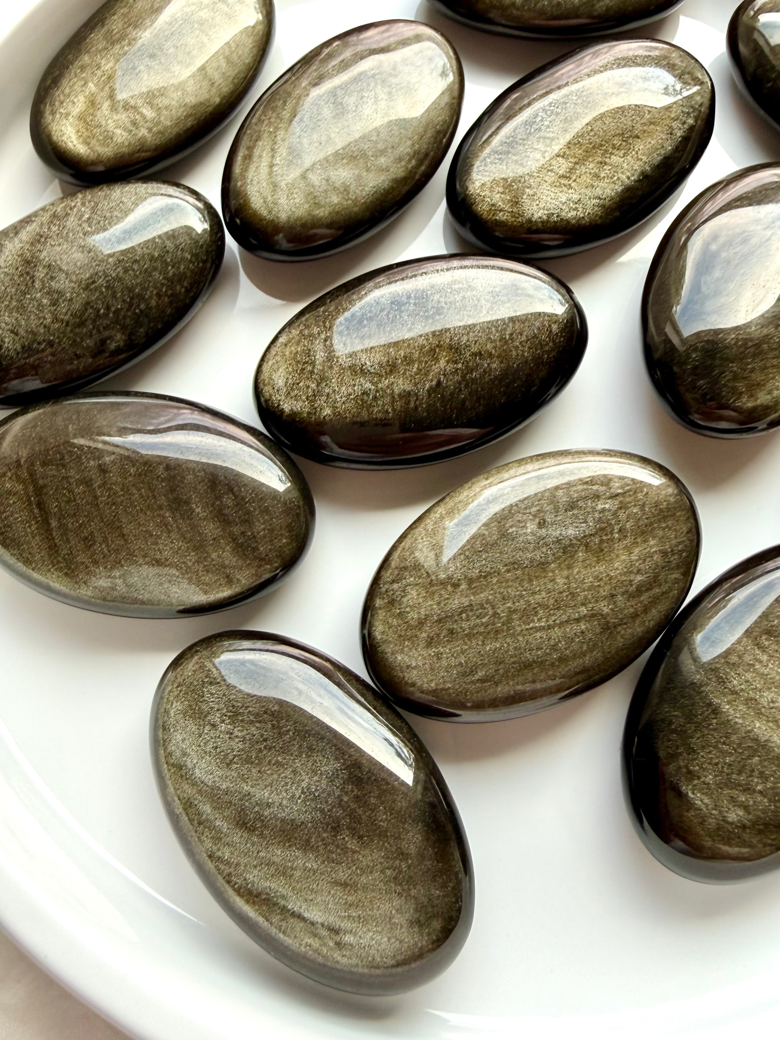Golden Sheen Obsidian crystals showing luminous metallic shimmer and natural flowing patterns across polished oval palm stones