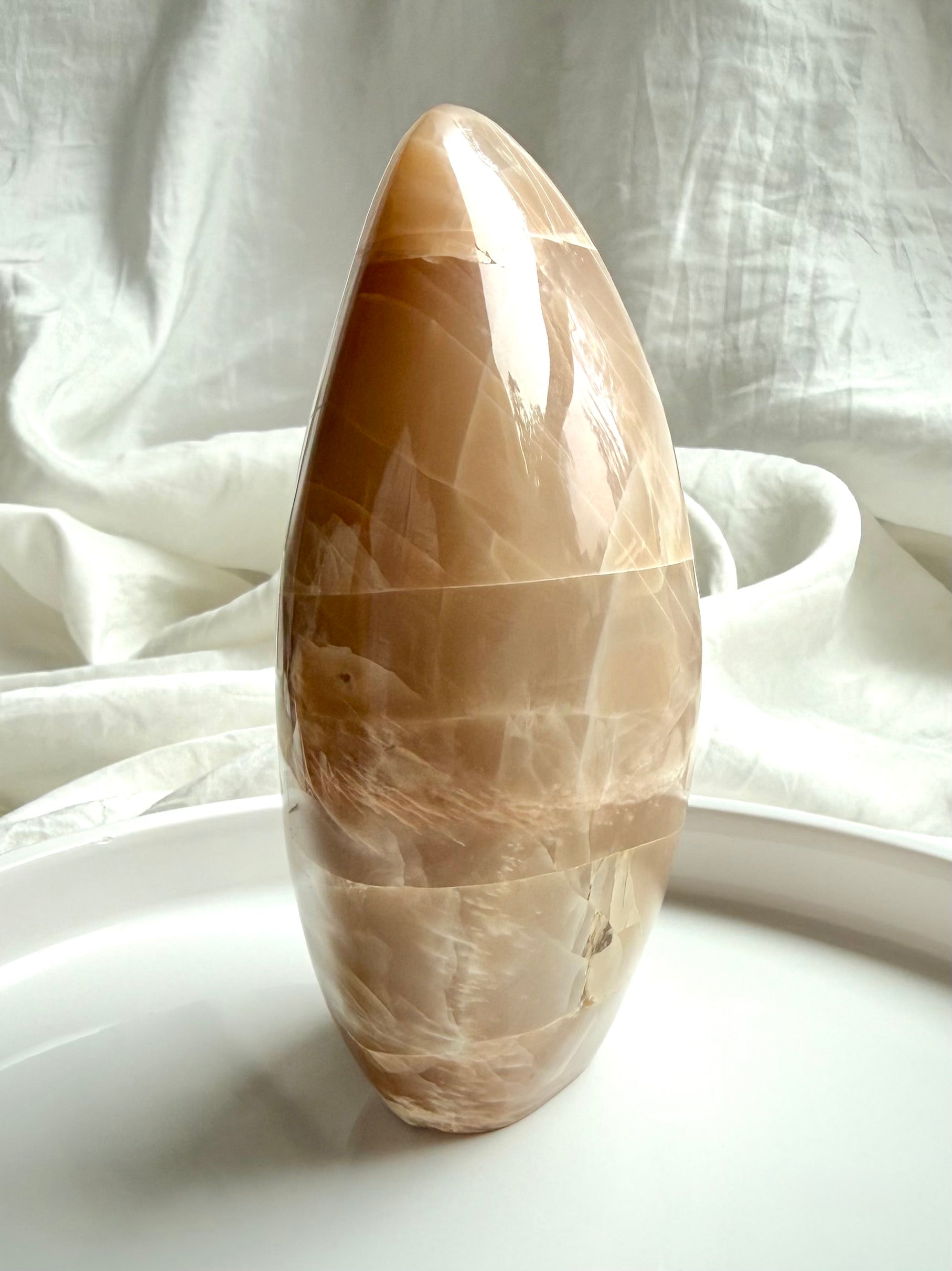 Side view of Peach Moonstone freeform crystal with soft shimmer and polished curved oval shape