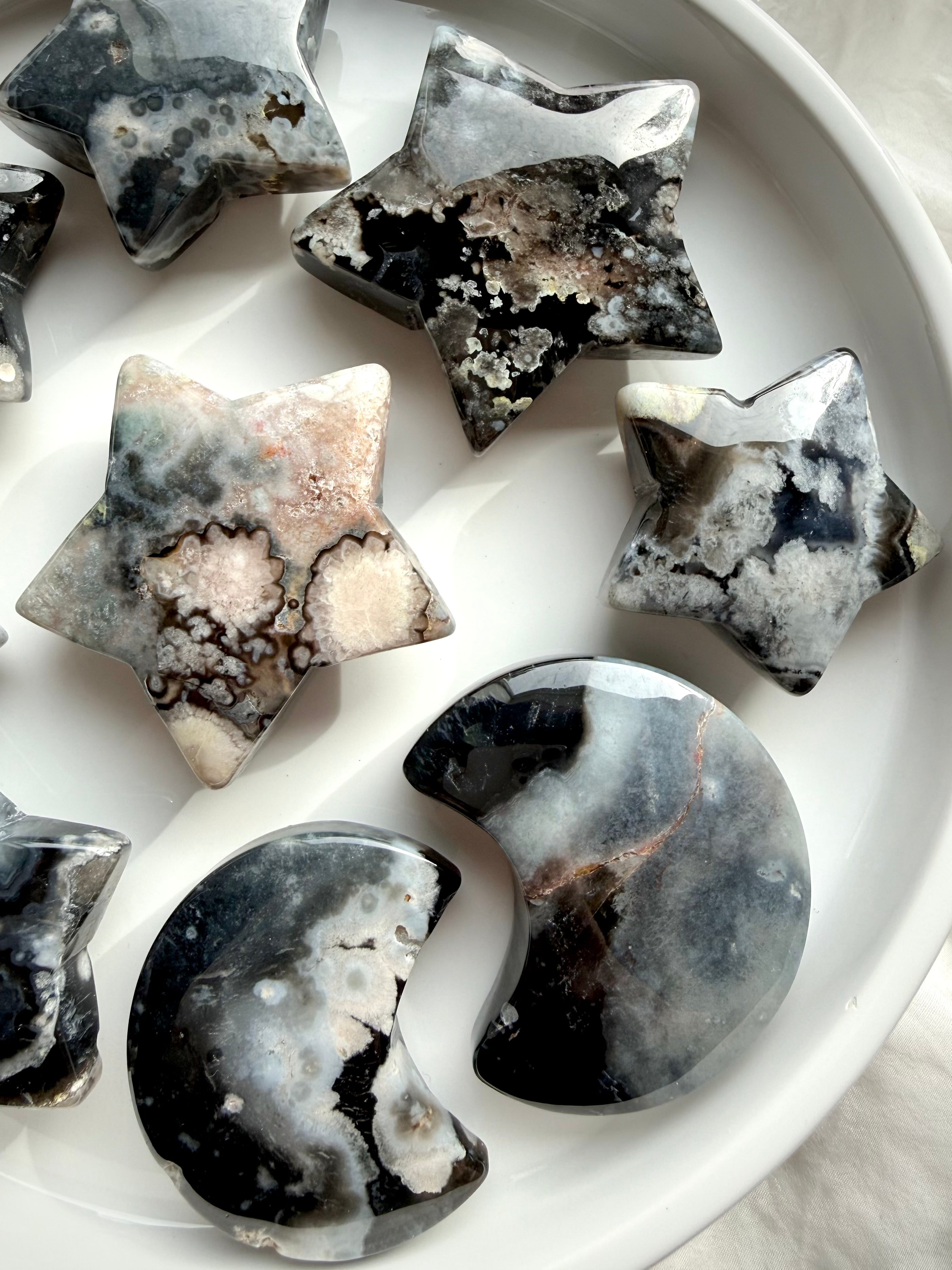 assortment of black flower agate moon and star crystals arranged together highlighting unique natural patterning