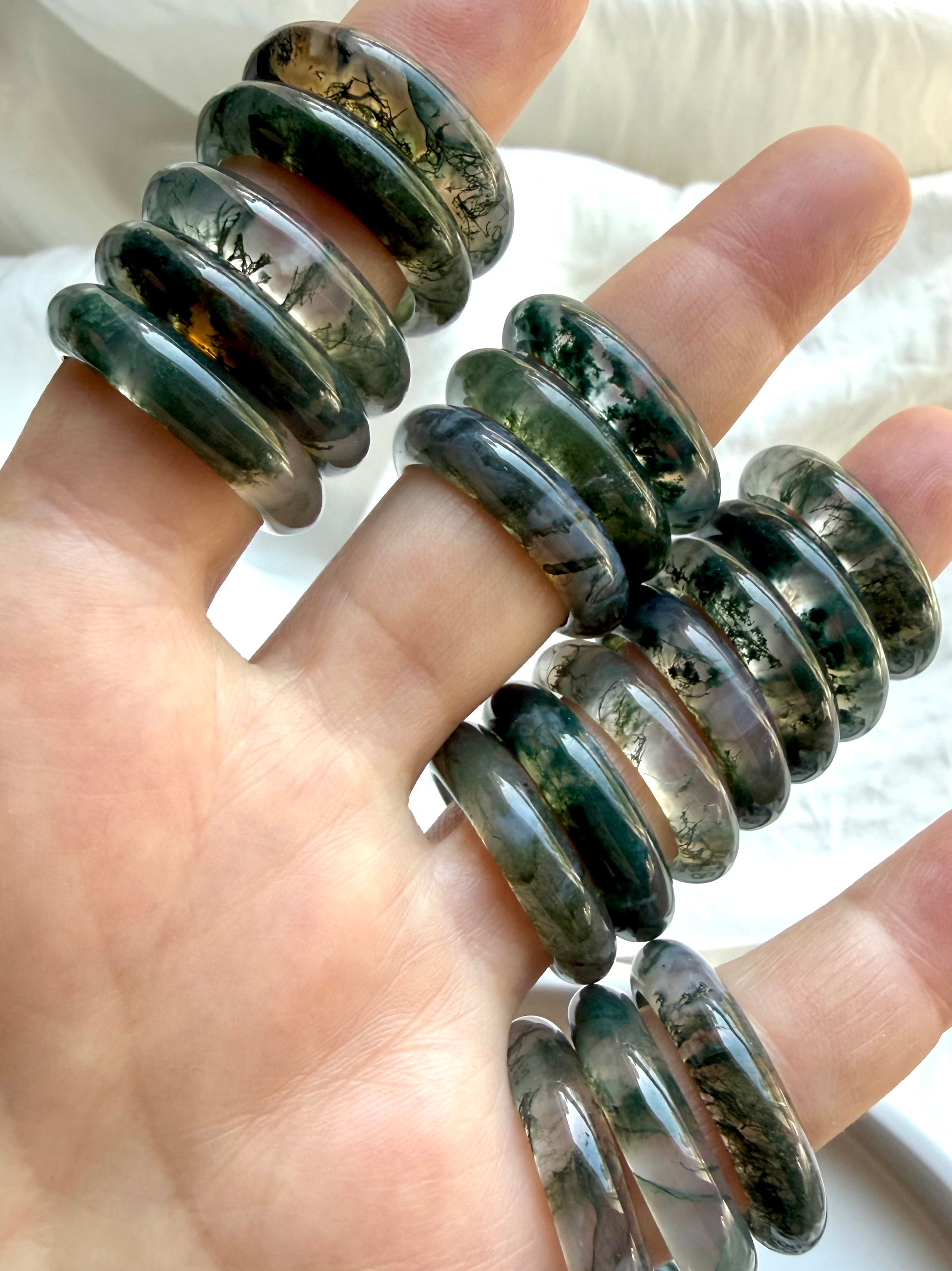 multiple moss agate band rings held in hand showing natural variation, polished crystal rings for balance growth and emotional healing