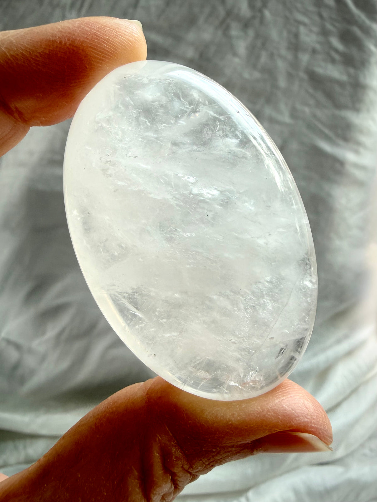 Clear Quartz palm stone held in hand showing translucent crystal, wispy white veils and natural internal formations