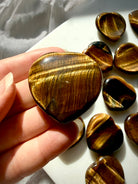 Golden Tiger’s Eye heart worry stones displayed in sunlight, showing natural chatoyancy and polished heart-shaped carvings 