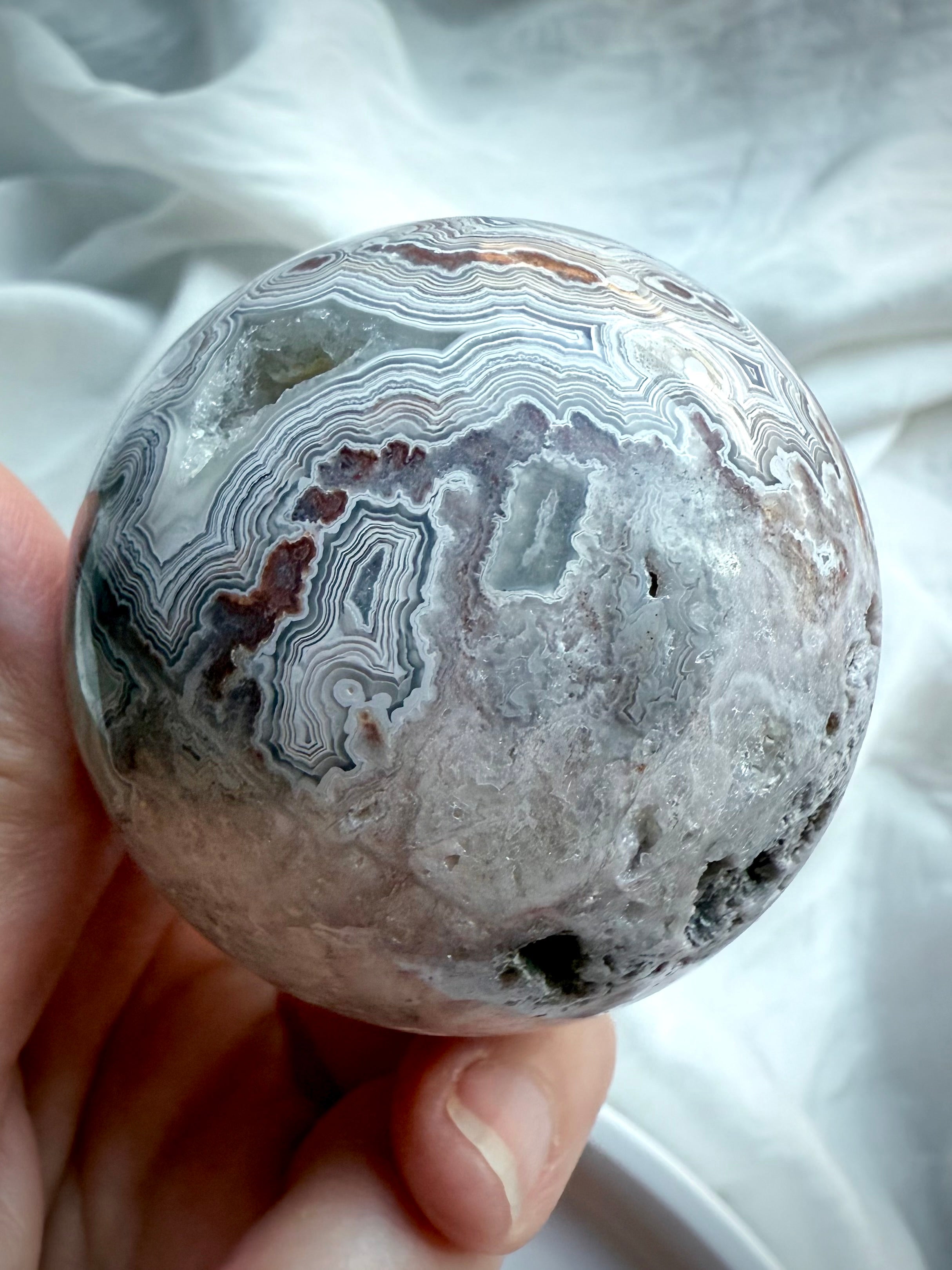 Natural agate crystal sphere with swirling bands, crystalline pockets, and earthy neutral tones for grounding energy work