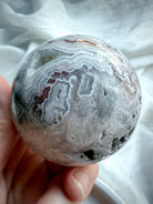 Natural agate crystal sphere with swirling bands, crystalline pockets, and earthy neutral tones for grounding energy work