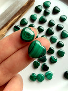 Two Malachite mini heart carvings held on my fingertips to show size and pattern detail.