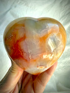 One-of-a-kind Carnelian heart crystal held in hand showing glossy polish, natural banding and scale