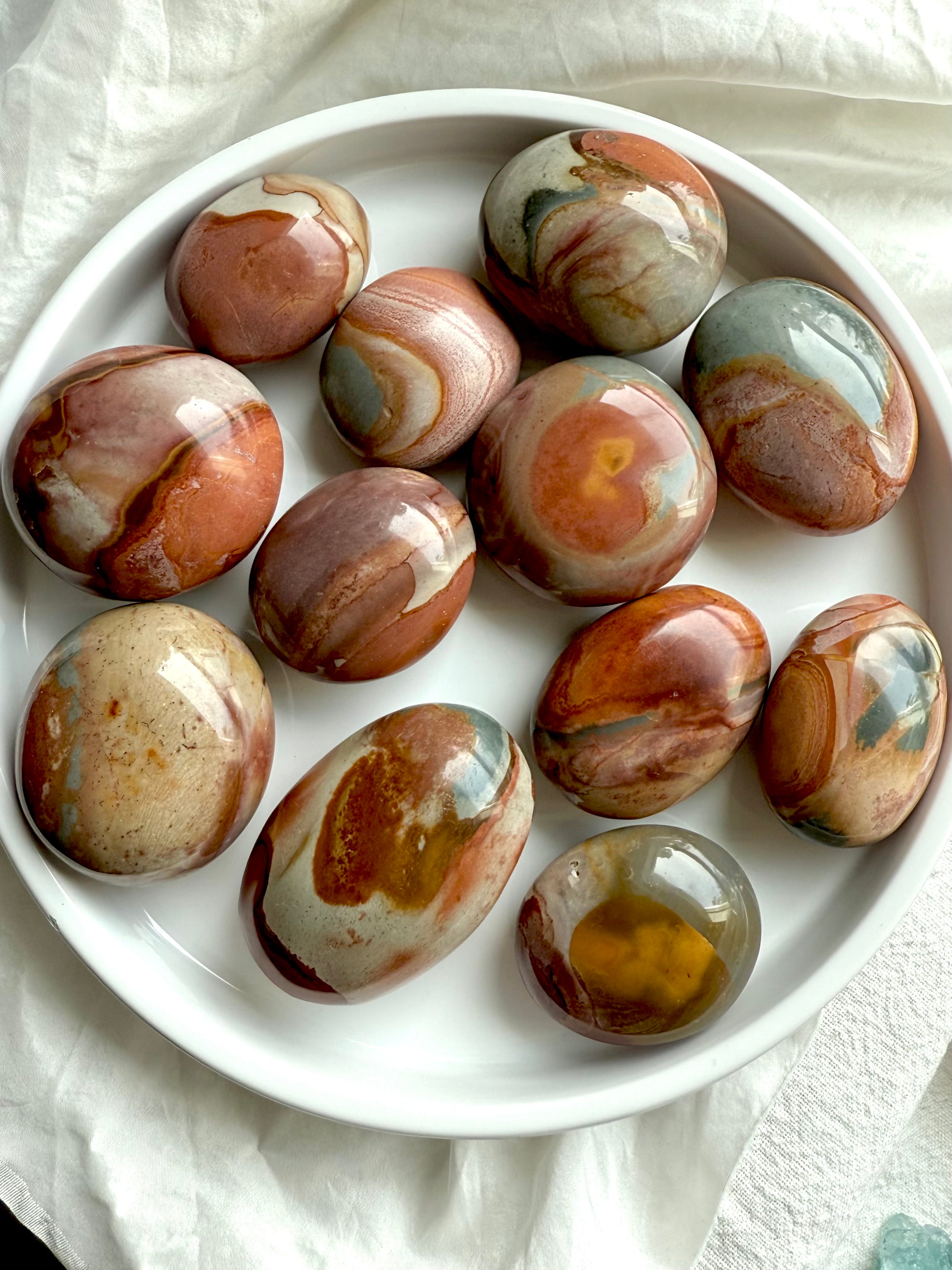 Earthy Polychrome Jasper palm stones on a plate, showcasing swirled color patterns & calming energy.