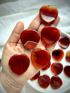 Carnelian heart worry stones held in hand showing natural color, translucency and pattern variation