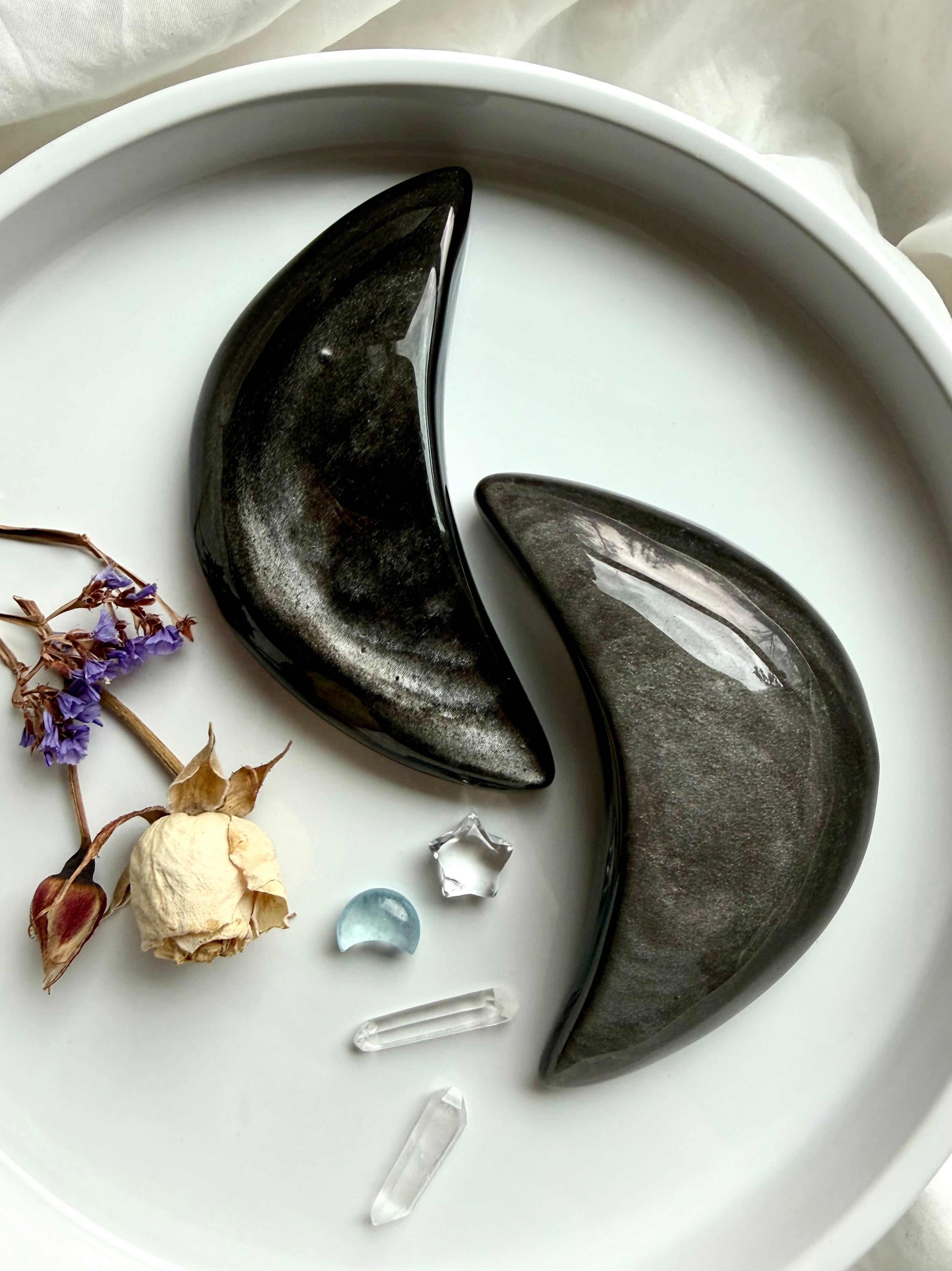 Silver Sheen Obsidian crescent moon carvings on white altar tray with dried flowers and gems, protective crystal for insight, grounding, and spiritual reflection
