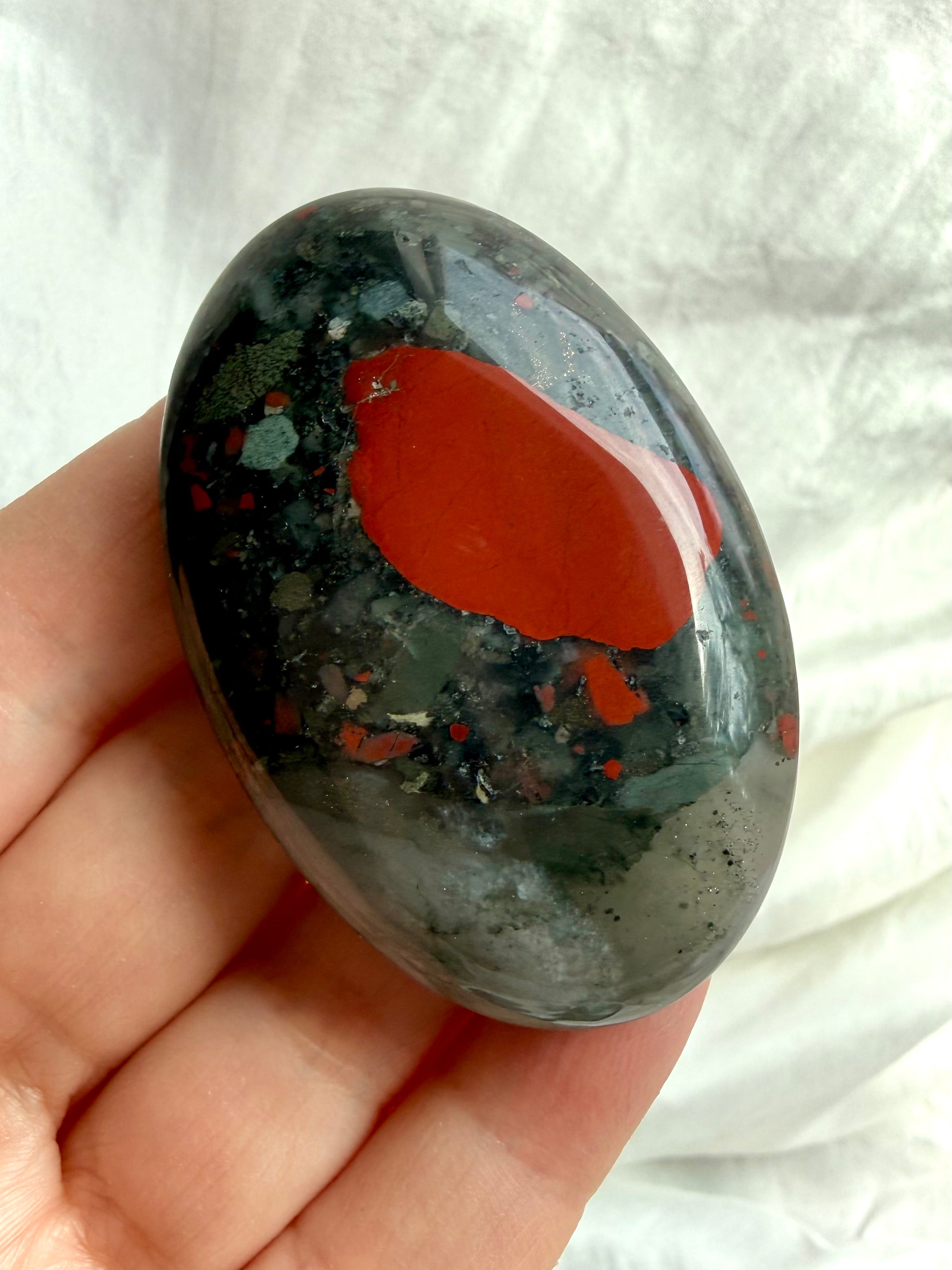 Polished Bloodstone palm stone showing a bold red inclusion, dark green matrix and subtle natural translucence