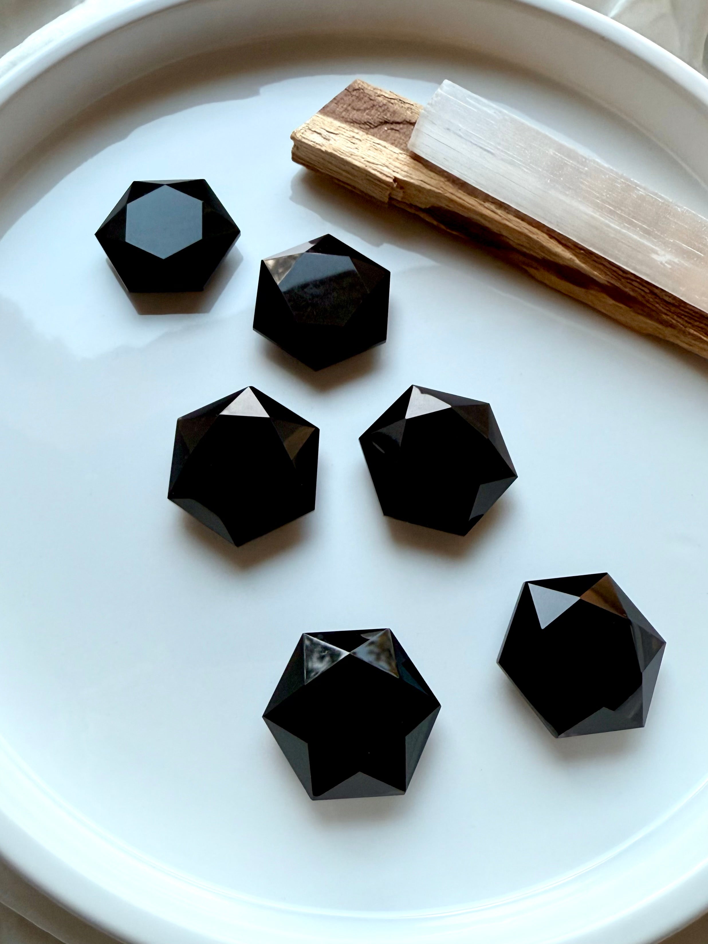 Polished Black Obsidian faceted hexagons arranged on a white dish beside Palo Santo — protective root chakra crystals for grounding and energetic shielding.